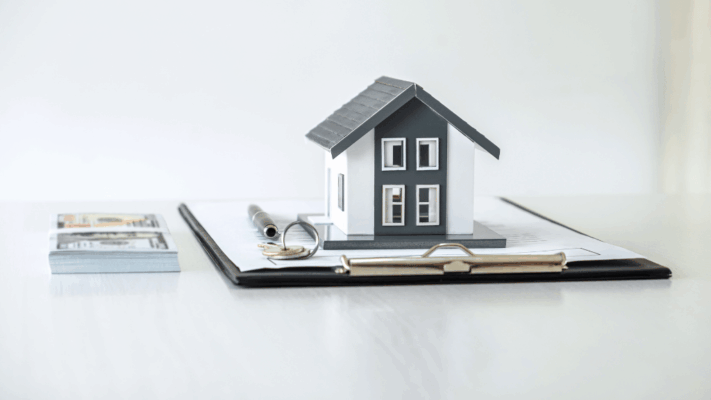 Model house, cash, and contract documents on a desk representing real estate syndication investments and investor qualification requirements
