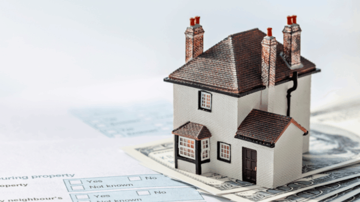 Miniature residential house model placed on top of U.S. dollar bills and financial paperwork, representing advanced real estate deal structuring, property financing, real estate syndications, investment capital planning, multifamily acquisitions, housing investment strategies, mortgage and funding analysis, commercial property transactions, and wealth-building through real estate investments.