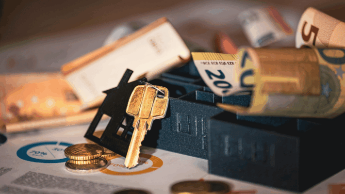 A close-up real estate finance scene featuring house keys, a miniature property model, coins, rolled cash, and financial charts spread across a desk, symbolizing advanced financial metrics every Albany NY investor should master. The image represents passive real estate investing, investment performance analysis, cash flow evaluation, ROI calculations, real estate syndication metrics, property financing strategies, wealth-building through multifamily investments, and financial literacy for commercial real estate investors.
