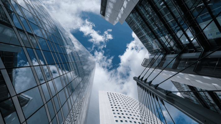 Upward view of modern commercial real estate buildings and glass office towers against a blue sky with clouds
