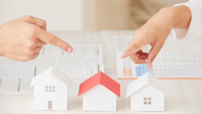 Two people comparing real estate investment options with model houses and financial documents during a property evaluation meeting
