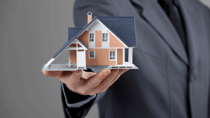 Business professional holding a model house, representing real estate syndication investments and property investment opportunities