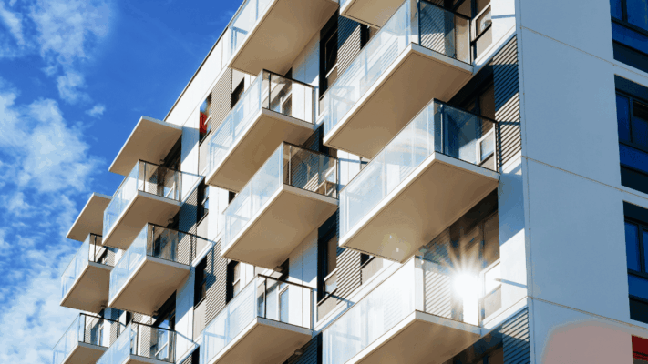 Modern multifamily apartment building with glass balconies and contemporary architecture under a bright blue sky 