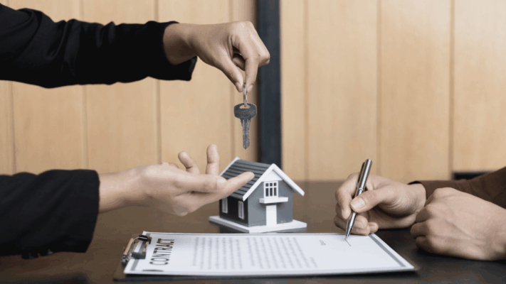 A professional real estate transaction scene featuring a person signing a property contract while another hands over a key above a miniature house model, symbolizing a real estate market forecast for Albany NY investors. The image represents property acquisition trends, passive real estate investing, market outlook analysis, investment timing, real estate syndication opportunities, housing market predictions, financial planning, and strategic decision-making for multifamily and commercial property investors.