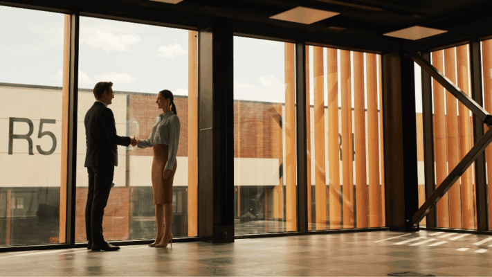 Two business professionals shaking hands inside a modern commercial property with large glass windows and warm natural lighting, symbolizing passive real estate investing partnerships, tax advantages of real estate investing in New York, commercial property agreements, investment collaboration, strategic financial planning, passive income opportunities, real estate syndication partnerships, investor relations, property acquisition deals, and long-term wealth-building through commercial real estate.
