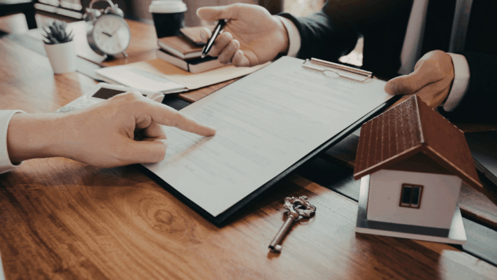 Real estate professionals reviewing property investment documents with a model house and keys during a cap rate analysis meeting
