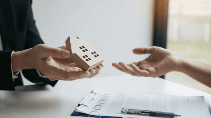 A professional real estate transaction scene showing a small house model being handed between two people above a visible contract document and pen, symbolizing due diligence in Albany syndication deals. The image represents property evaluation, investment verification, real estate syndication analysis, passive investment decision-making, contract review, financial transparency, risk assessment, and careful examination of multifamily real estate opportunities before investing. 