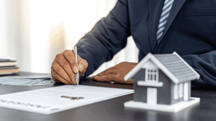 Business professional signing financial documents beside a miniature house model, representing advanced cash flow optimization, real estate investment management, property financing strategies, commercial real estate investing, rental income planning, financial analysis, real estate syndication, wealth-building through property assets, investment performance optimization, and strategic real estate financial planning.