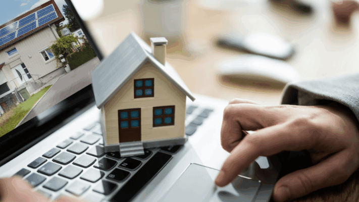A modern real estate investment planning scene featuring a miniature house model placed on a laptop keyboard while an investor reviews digital property listings, symbolizing passive investment liquidity planning for Albany NY investors. The image represents online real estate analysis, passive investing strategies, liquidity planning, portfolio management, real estate syndication, digital investment research, multifamily property evaluation, financial flexibility, and long-term wealth planning for commercial real estate investors.