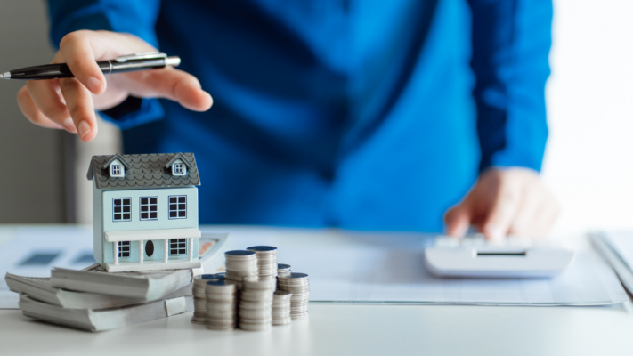 A miniature house sits on stacks of cash beside neatly arranged coins while a person reaches toward it with a pen and works with a calculator in the background. The composition emphasizes evaluating the financial side of real estate before making an investment decision. It works well for topics such as **common investment mistakes new real estate investors make**, budgeting for investment properties, financial planning, cash flow analysis, due diligence, investment strategy, property valuation, financing decisions, ROI calculations, and avoiding costly real estate investing errors.
