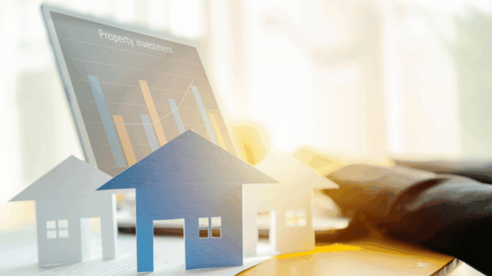 A modern real estate investment planning concept featuring paper house models in front of a digital investment dashboard displaying property performance charts and financial analytics. The image represents creating a passive real estate investment plan, multifamily investing, portfolio planning, investment strategy, financial goal setting, property analysis, passive income, commercial real estate education, long-term wealth building, and developing a structured roadmap for your first passive real estate investment.