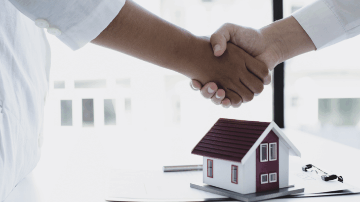 A professional real estate investment scene featuring two parties shaking hands beside a model home, symbolizing trust, partnership, and successful investment decisions. The image represents comparing passive real estate investment opportunities, evaluating multifamily syndication deals, sponsor selection, due diligence, investment strategy, risk versus return analysis, commercial real estate partnerships, investor confidence, and making informed passive investment decisions through careful opportunity comparison.