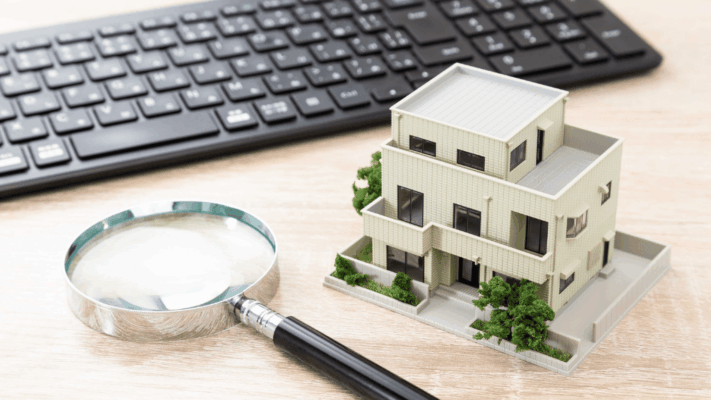 A real estate investment analysis scene featuring a modern residential building model beside a magnifying glass and computer keyboard, symbolizing how to evaluate exit strategies in Albany NY syndication investments. The image represents passive real estate investing, investment exit planning, property valuation, due diligence, multifamily syndication analysis, portfolio optimization, financial decision-making, asset disposition strategies, and long-term wealth management for commercial real estate investors.