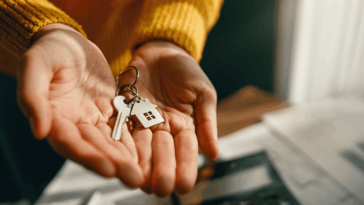 A close-up of a hand holding house keys with a home-shaped keychain, symbolizing new investment opportunities and property ownership. The image represents identifying emerging multifamily markets, commercial real estate investing, market research, passive investment opportunities, property acquisition, strategic market selection, portfolio expansion, real estate growth potential, investment readiness, and discovering promising multifamily markets around Albany NY.