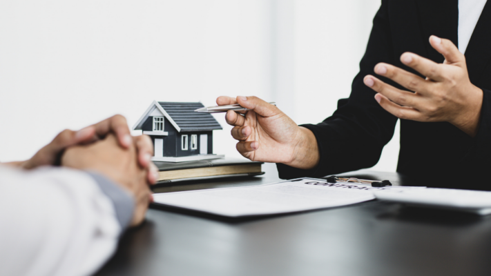 A real estate professional discusses investment performance with a client, using a model home and contract documents to explain key property metrics and financial results. The image highlights communication, analysis, and strategic decision-making, making it ideal for topics such as **key performance indicators every multifamily investor should know**, multifamily investment analysis, occupancy rates, net operating income (NOI), cash flow, expense ratios, investor reporting, asset management, property performance, and tracking long-term real estate investment success.
