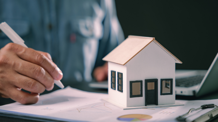 A person reviews financial documents beside a model home, with a laptop in the background, representing the careful analysis of a property's financial performance. The image emphasizes evaluating income, expenses, and key financial metrics before making investment decisions. It is ideal for topics such as **understanding a multifamily property financial statement**, multifamily financial analysis, net operating income (NOI), cash flow evaluation, operating expenses, due diligence, asset management, real estate underwriting, investment performance, and making informed multifamily investment decisions.
